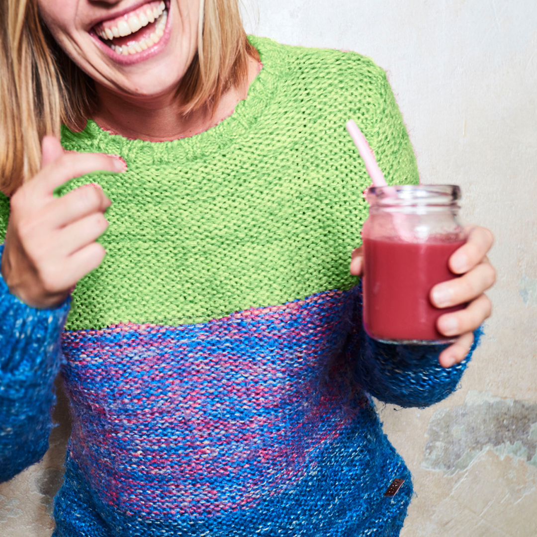 girl in colorful sweater holding berry smoothie in mason jar