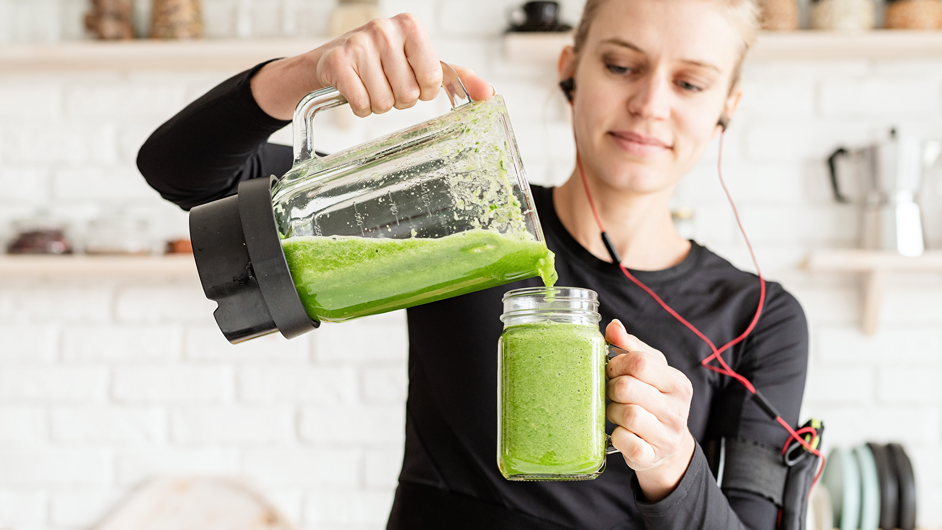 girl with headphones making green smoothie with blender 